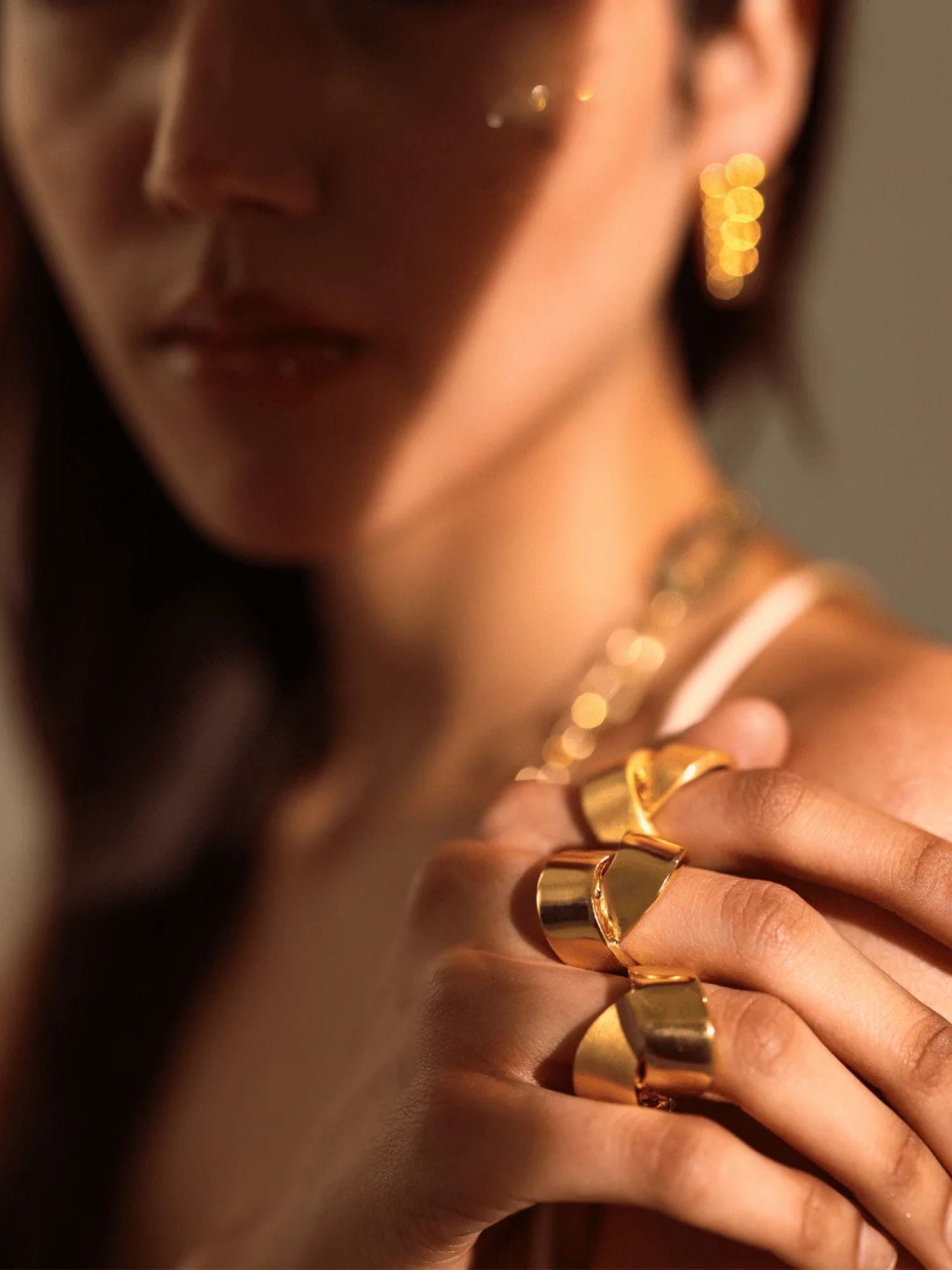 Close-up of model's fingers wearing sculptural gold ribbon ring in warm light